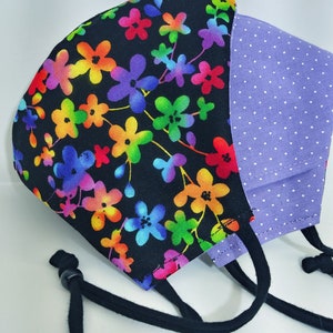 May include: A black face mask with a rainbow floral print on one side and a purple polka dot print on the other side. The mask has black ties.
