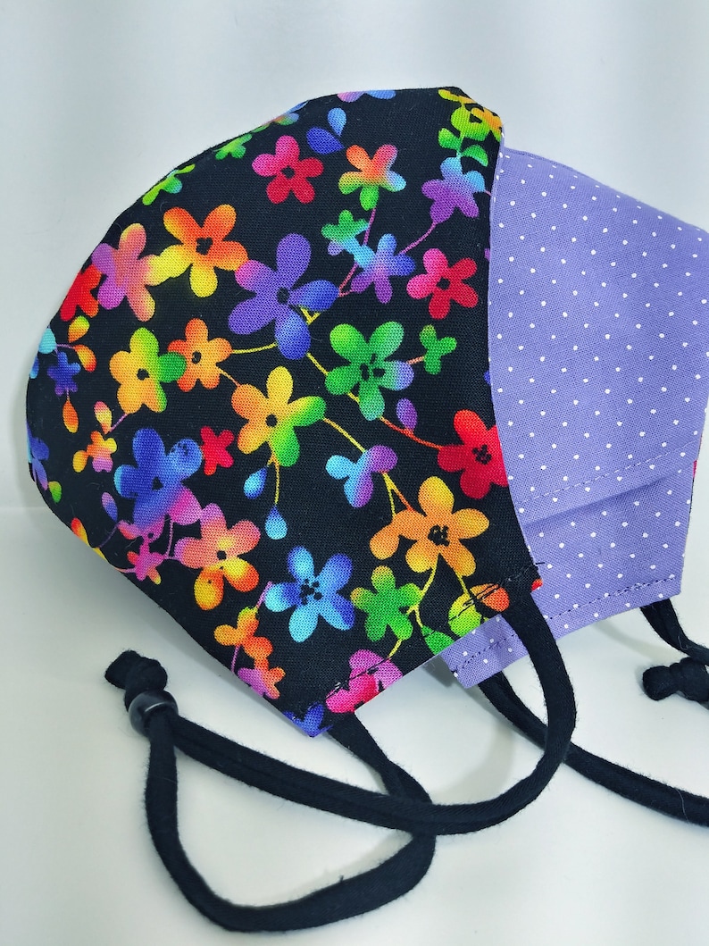 May include: A black face mask with a rainbow floral print on one side and a purple polka dot print on the other side. The mask has black ties.