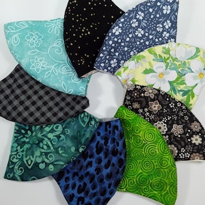 May include: A collection of nine fabric face masks in various patterns, including floral, geometric, and abstract designs. The masks are all in different colors, including green, blue, black, and white.