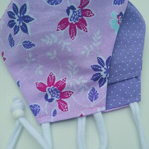 May include: A purple and white floral fabric face mask with a purple polka dot fabric lining. The mask has white elastic ear loops.