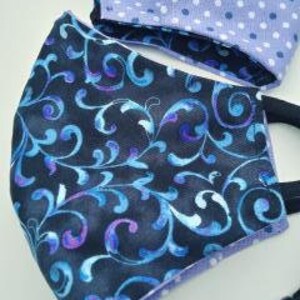 May include: Two face masks, one with a black background and a blue and purple floral pattern, and the other with a light purple background and white polka dots.