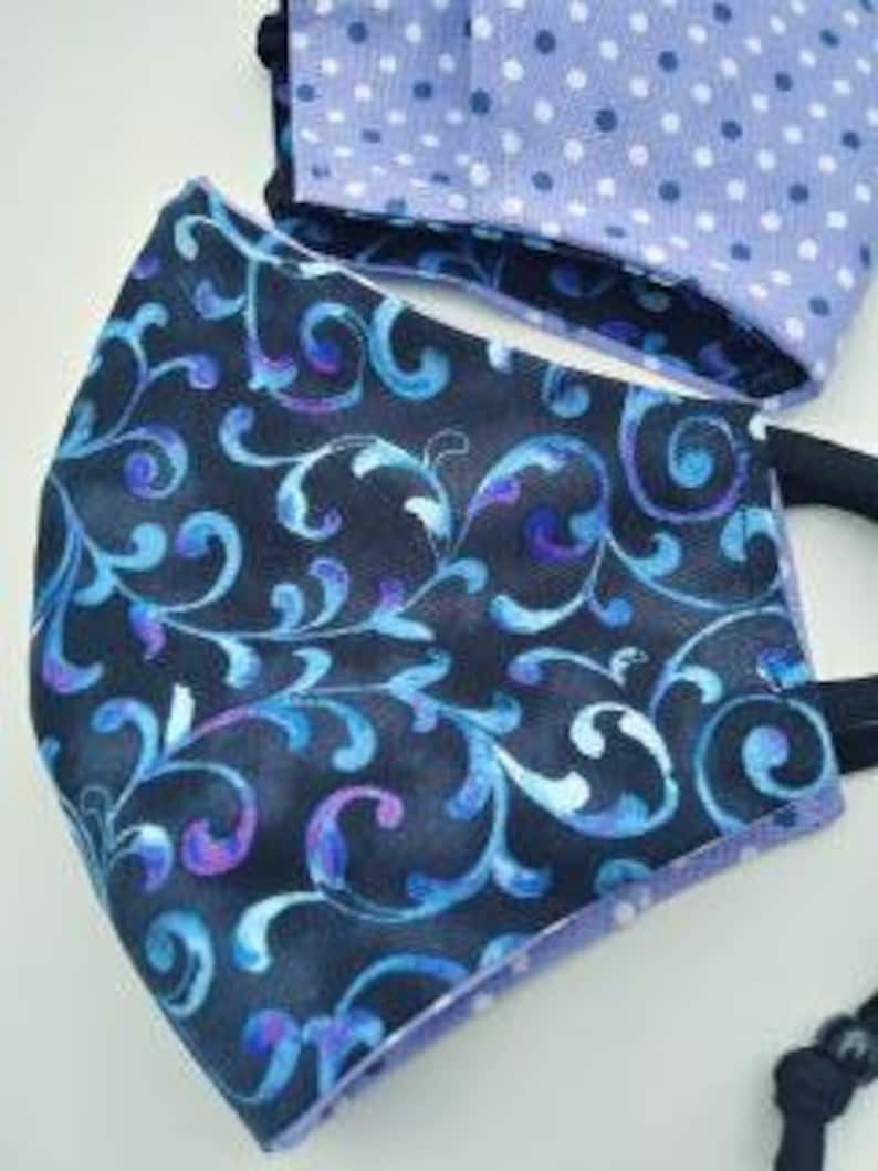 May include: Two face masks, one with a black background and a blue and purple floral pattern, and the other with a light purple background and white polka dots.