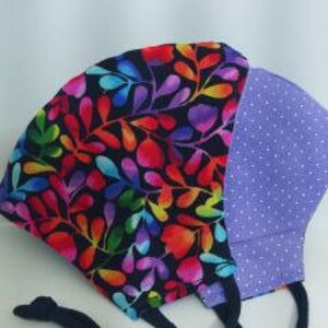 May include: A reusable face mask with a black background and a colorful floral pattern on one side and a purple polka dot pattern on the other side. The mask has black elastic ear loops.