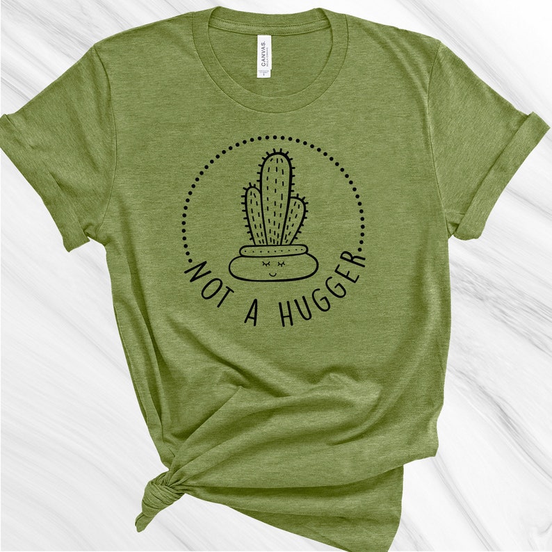 Puede incluir: Una camiseta verde con un gr&aacute;fico de cactus negro y el texto "Not a Hugger" en un c&iacute;rculo.