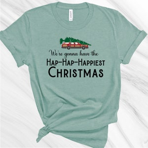 May include: A teal blue t-shirt with a Christmas tree and a red station wagon printed on the front. The text "We're gonna have the HAP-HAP-HAPPIEST CHRISTMAS" is printed below the image.