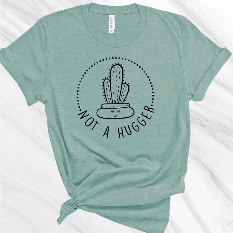 Puede incluir: Una camiseta verde claro con un gr&aacute;fico de cactus negro y el texto "Not a Hugger" en un c&iacute;rculo.