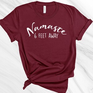 May include: A maroon t-shirt with white text that reads "Namaste 6 feet away".