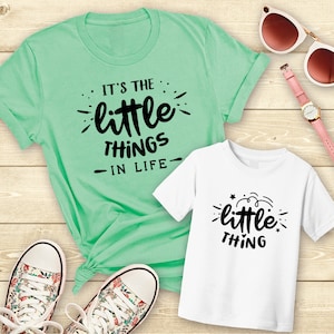 May include: A set of two t-shirts, one green and one white, with the text "It's the little things in life" and "little thing" printed on them.
