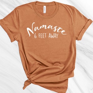 May include: A brown t-shirt with the text "Namaste 6 feet away" printed in white.