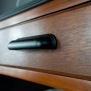 May include: Close-up of a wooden drawer with a black metal pull handle. The drawer is part of a dresser or cabinet.