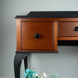 May include: A vintage wooden desk with black painted legs and drawers. The desk has a black top and wooden drawers with black knobs.