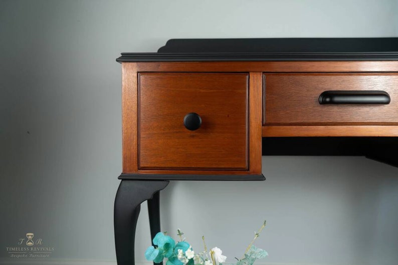May include: A vintage wooden desk with black painted legs and drawers. The desk has a black top and wooden drawers with black knobs.