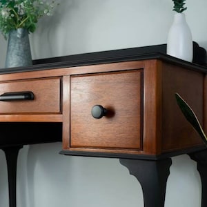May include: A black and wood console table with three drawers and four legs. The table has black knobs and a black top.