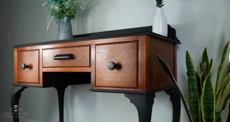 May include: A black and wood console table with three drawers and four legs. The table has black knobs and a black top.