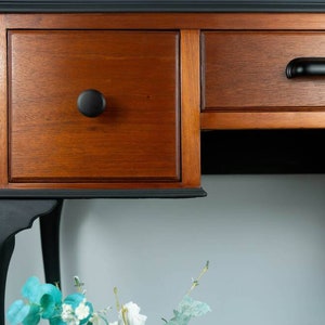 May include: A wooden desk with two drawers and black painted legs. The top of the desk is painted black, and the drawers are a natural wood color. The desk has a simple, elegant design.