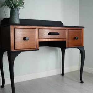 May include: A black and wood vanity table with three drawers and cabriole legs. The table has a black top and black legs with a wood base.