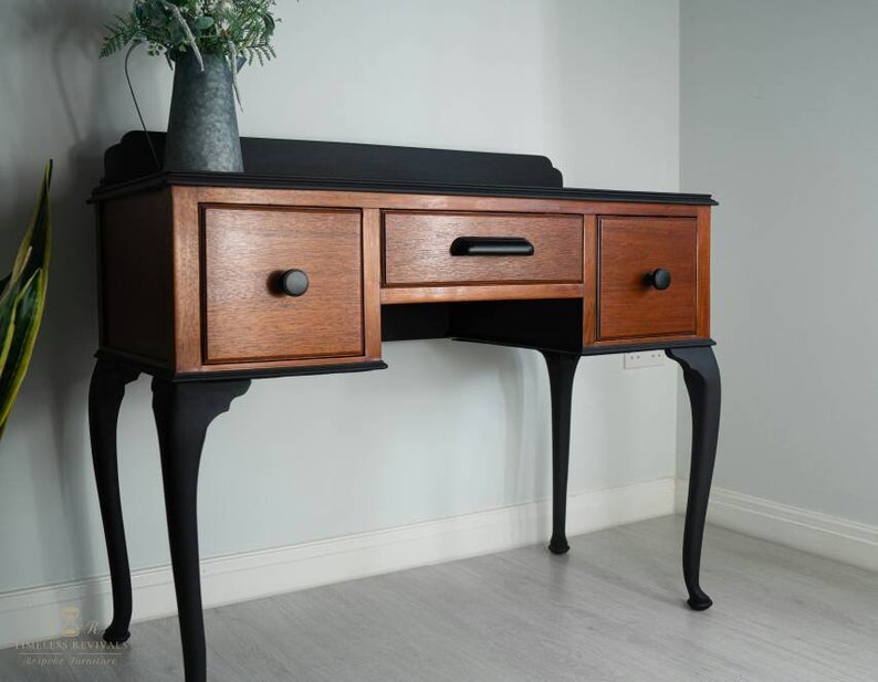 May include: A black and wood vanity table with three drawers and cabriole legs. The table has a black top and black legs with a wood base.