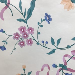 May include: A white wallpaper featuring a repeating pattern of pink ribbons, dark teal stems, and clusters of small flowers in shades of pink, blue, and light orange. The design includes delicate green leaves and small blue buds on thin, curved vines.