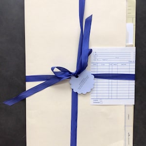 May include: A set of cream-colored file folders tied together with a blue ribbon. The folders have a blue and white label with the text "THIS IS" and a blue and white label with the text "CASH CHARGE".