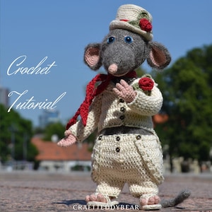 May include: Crocheted rat wearing a white hat with a red rose, a red scarf, and a white crocheted outfit with red roses. The rat is standing on a brick surface. The text "Crochet Tutorial" is visible in the background.