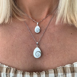 Könnte beinhalten: Zwei silberne Halsketten mit einem weißen Muschel-Anhänger mit grünem Spiralmuster. Die Halsketten sind übereinander auf dem Hals einer Person gelegt.