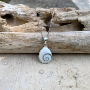May include: A silver chain necklace with a white shell pendant featuring a spiral pattern. The pendant is shaped like a teardrop.