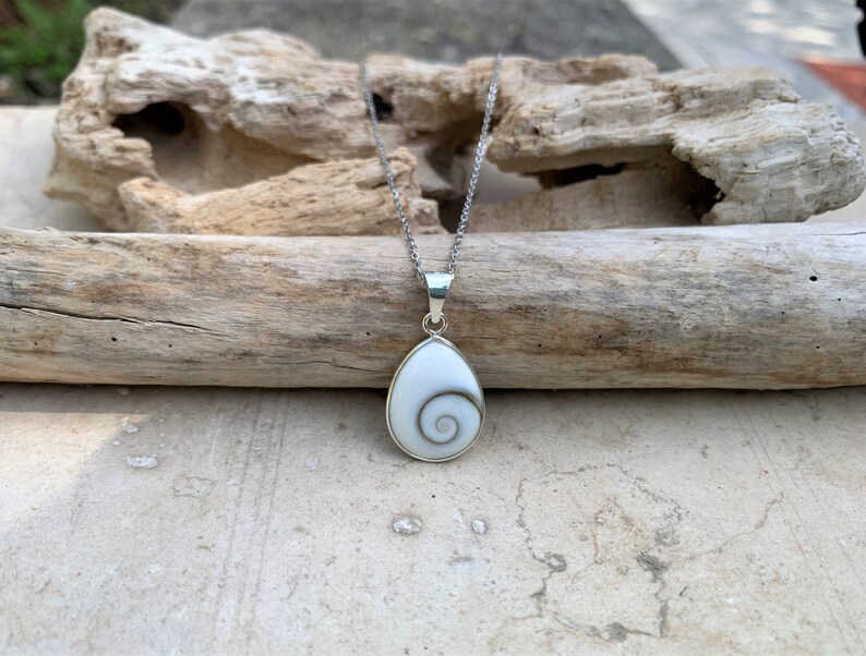 May include: A silver chain necklace with a white shell pendant featuring a spiral pattern. The pendant is shaped like a teardrop.