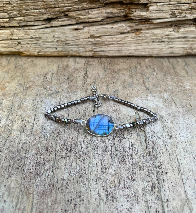 Puede incluir: Un brazalete de plata con una piedra preciosa de labradorita azul y cuentas de hematites negras.