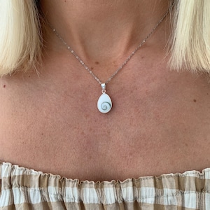 May include: A silver chain necklace with a white shell pendant featuring a green spiral design.