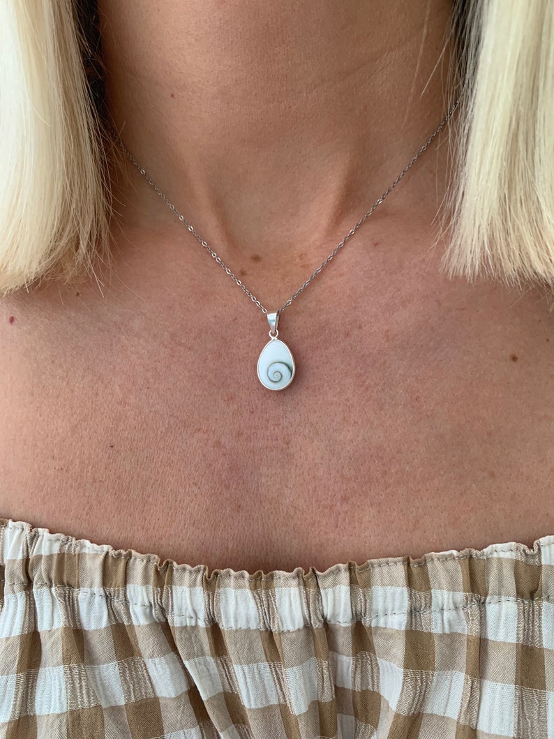 May include: A silver chain necklace with a white shell pendant featuring a green spiral design.