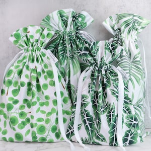 Puede incluir: Cuatro bolsas blancas de cord&oacute;n con estampados de hojas verdes. Las bolsas est&aacute;n hechas de algod&oacute;n y tienen cordones blancos. Las bolsas tienen todas diferentes estampados, una con un estampado de hojas grandes, otra con un estampado de hojas peque&ntilde;as y dos con un estampado de c&iacute;rculos peque&ntilde;os.