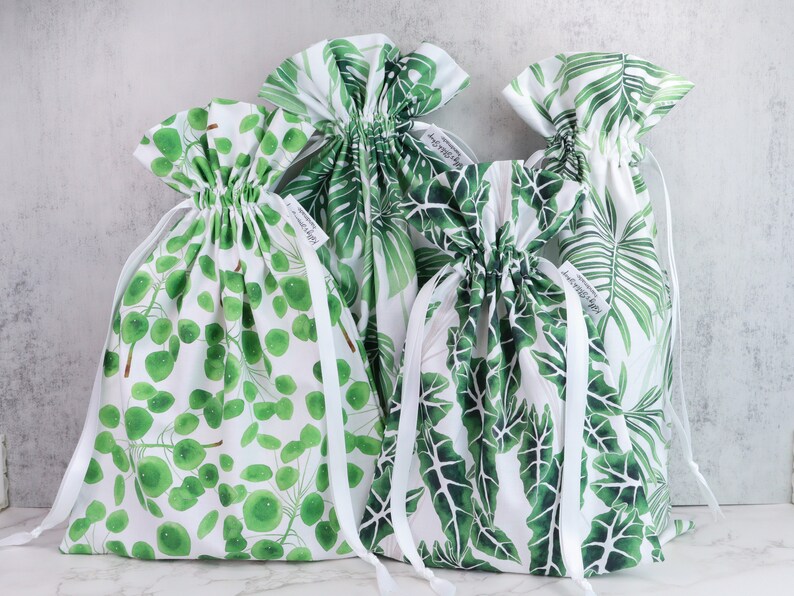 Puede incluir: Cuatro bolsas blancas de cord&oacute;n con estampados de hojas verdes. Las bolsas est&aacute;n hechas de algod&oacute;n y tienen cordones blancos. Las bolsas tienen todas diferentes estampados, una con un estampado de hojas grandes, otra con un estampado de hojas peque&ntilde;as y dos con un estampado de c&iacute;rculos peque&ntilde;os.