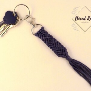 May include: A dark purple braided key chain with a tassel. The keychain is attached to a silver key ring with keys.