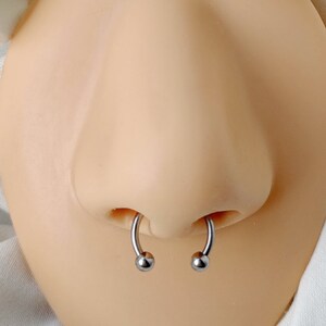 Pu&ograve; includere: Primo piano di un piercing al naso con due anelli d'argento. Gli anelli sono circolari con piccole sfere ad ogni estremit&agrave;.