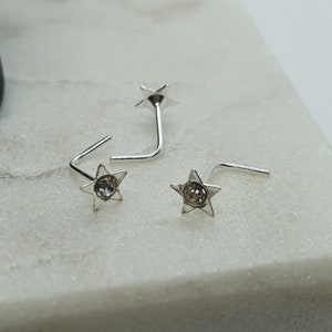 May include: Three silver nose rings with a star design and a clear rhinestone in the centre of each star.