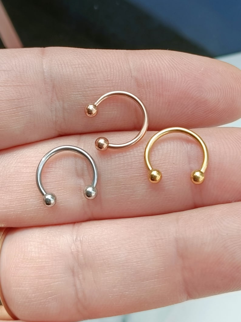 Pu&ograve; includere: Tre anelli per il naso a forma di ferro di cavallo con estremit&agrave; a sfera. Gli anelli sono argento, oro e oro rosa.