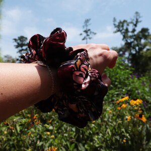May include: A burgundy and floral patterned scrunchie with a gold chain bracelet on a person's wrist.