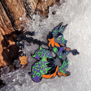 Puede incluir: Un pin de esmalte negro, verde y naranja de un zorro de dibujos animados sosteniendo un bastón con una linterna. El zorro tiene un patrón de remolino verde y morado en su cuerpo.