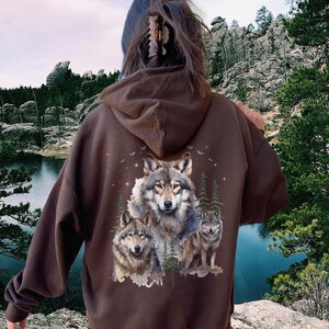 May include: A brown hooded sweatshirt with a graphic print of three wolves on the back. The sweatshirt is slightly oversized and has a dark chocolate color.