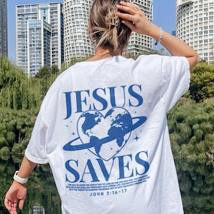 K&ouml;nnte beinhalten: Wei&szlig;es T-Shirt mit einer blauen Grafik eines Herzens mit einem Globus darin und einem Ring darum. Der Text "JESUS SAVES" befindet sich &uuml;ber der Grafik und "JOHN 3:16-17" unter der Grafik.