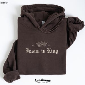 May include: A brown hoodie with a crown and the text "Jesus is King" in a vintage font. The text "Rev. 17:14" is above the crown.