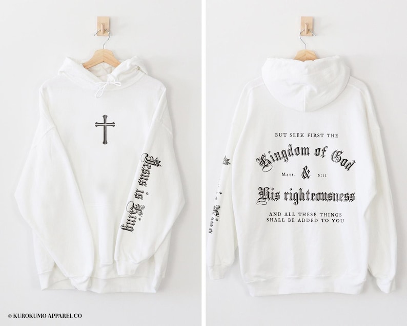 Op de afbeelding: Witte hoodie met een kruis op de voorkant en de tekst "Jesus is King" op de linkermouw. De achterkant van de hoodie heeft de tekst "But seek first the Kingdom of God & His righteousness and all these things shall be added to you".