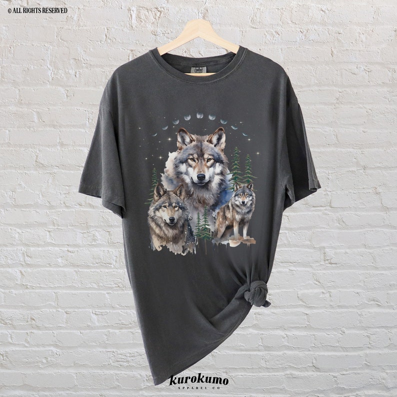 May include: A dark gray t-shirt with a graphic print of three wolves in a forest setting. The wolves are surrounded by trees and a crescent moon. The shirt is made of a soft, comfortable material.