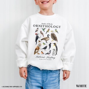 May include: White ornithology sweatshirt featuring a collection of illustrated birds. The text "Study of Birds, Ornithology, Natural History Collection" is printed above and below the bird illustrations. The sweatshirt is worn by a child.