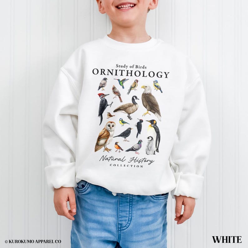 May include: White ornithology sweatshirt featuring a collection of illustrated birds. The text "Study of Birds, Ornithology, Natural History Collection" is printed above and below the bird illustrations. The sweatshirt is worn by a child.