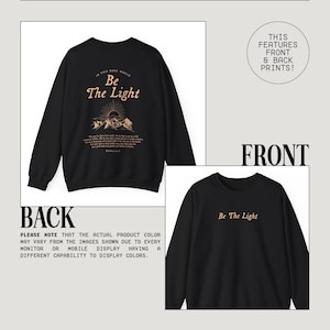 May include: Black sweatshirt with a front and back print. The front print says "Be The Light" in a light brown color. The back print says "In this dark world, Be The Light" with a mountain scene and a quote from Matthew 5:14-16 in a light brown color.