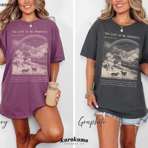 Puede incluir: Dos mujeres llevan camisetas de gran tama&ntilde;o con el texto "The Lord is my shepherd; Psalm 23:1-6" impreso en la parte delantera. Las camisetas est&aacute;n disponibles en dos colores: baya y grafito.