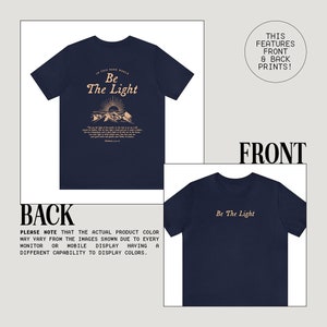 May include: Navy blue t-shirt with a front and back print. The front print says "Be The Light" in a light brown color. The back print features a mountain scene with a sun and the text "In this dark world, Be The Light" in a light brown color.