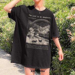Puede incluir: Camiseta negra de gran tama&ntilde;o con un estampado gr&aacute;fico de un paisaje con ovejas y el texto "The Lord is my shepherd; Psalm 23:1-3".