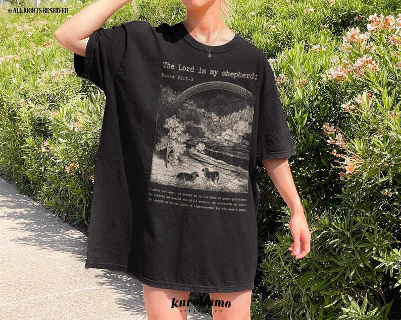 Puede incluir: Camiseta negra de gran tama&ntilde;o con un estampado gr&aacute;fico de un paisaje con ovejas y el texto "The Lord is my shepherd; Psalm 23:1-3".